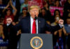 A man in a suit passionately speaking at a podium with a presidential seal, surrounded by a cheering crowd