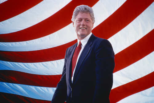 Bill Clinton smiling in front of an American flag