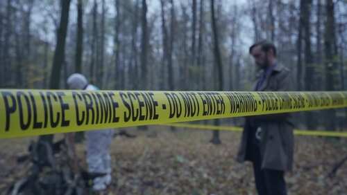 shutterstock_2454286645 (2).jpg Police crime scene tape in a forest with investigators