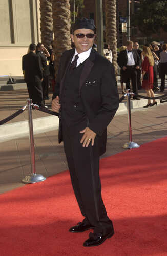 A man in a black suit and hat posing on a red carpet at an event