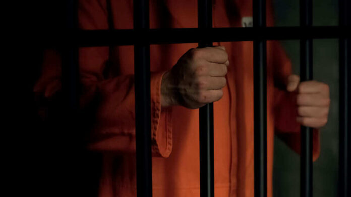 1486458806 Person in orange prison jumpsuit behind bars