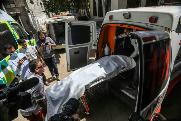 2445410825 People loading stretcher into ambulance surrounded by onlookers
