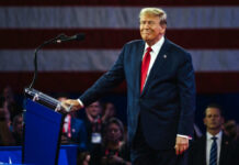 Man in suit at podium with American flag backdrop