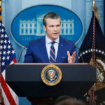 Man speaking at podium with US flags behind