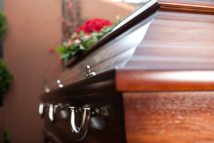 Close-up of a wooden casket adorned with flowers in a funeral setting