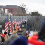 A speaker at a podium with American flags in the background addressing a crowd