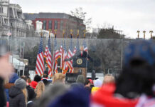 A speaker at a podium with American flags in the background addressing a crowd