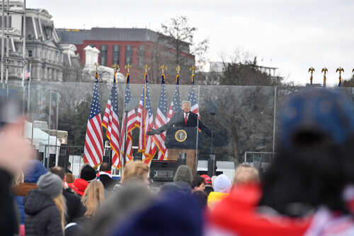 shutterstock_1890489670.jpg A speaker at a podium with American flags in the background addressing a crowd