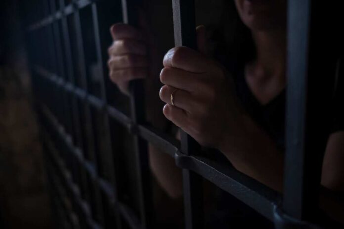 Hands gripping prison bars in a dimly lit environment