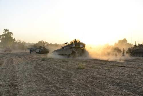 shutterstock_2372752981.jpg Military tanks moving through a dusty field at sunset