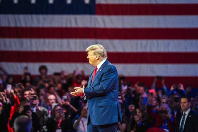 shutterstock_2455398339.jpg A speaker on stage in front of an American flag at a political rally