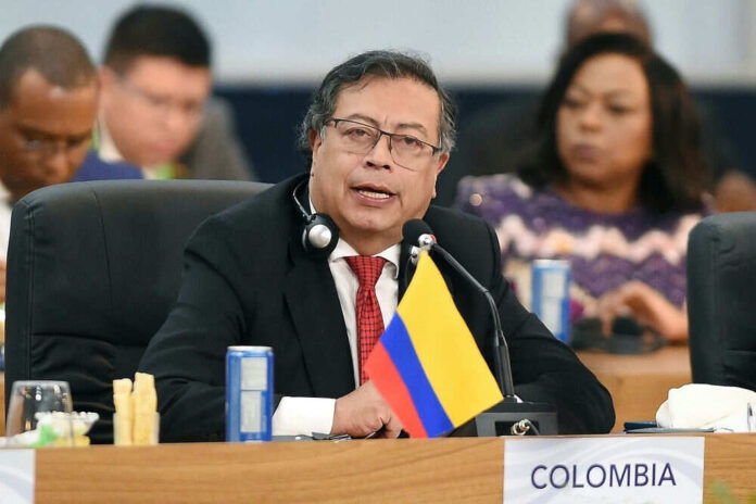 Man speaking at conference with Colombia flag present