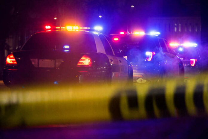 Police cars with flashing lights behind caution tape