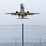 Airplane taking off above a wire fence
