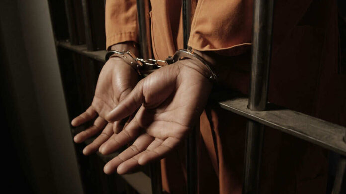 Person handcuffed behind prison bars in orange jumpsuit