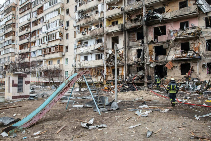 Damaged apartment building with debris and firefighters nearby