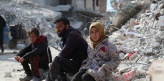 A man, a boy, and a girl sitting on rubble in a devastated area