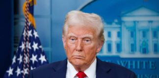 A political figure standing in front of the American flag during a press briefing
