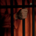 Self-Mutilation Plot? Jury Didn’t Buy It Person in orange prison jumpsuit behind bars