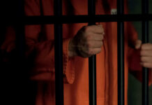 Person in orange prison jumpsuit behind bars