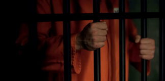 Person in orange prison jumpsuit behind bars